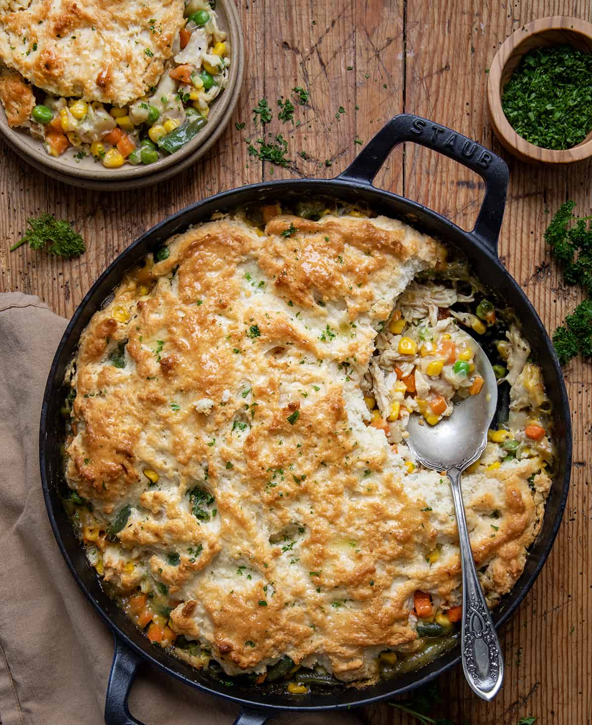 Bisquick Chicken Pot Pie in a skillet with some removed and a spoon in a skillet on a wooden table. 
