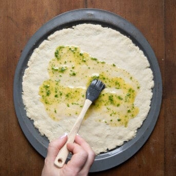 Brushing herb butter over raw Bisquick Pizza Dough.