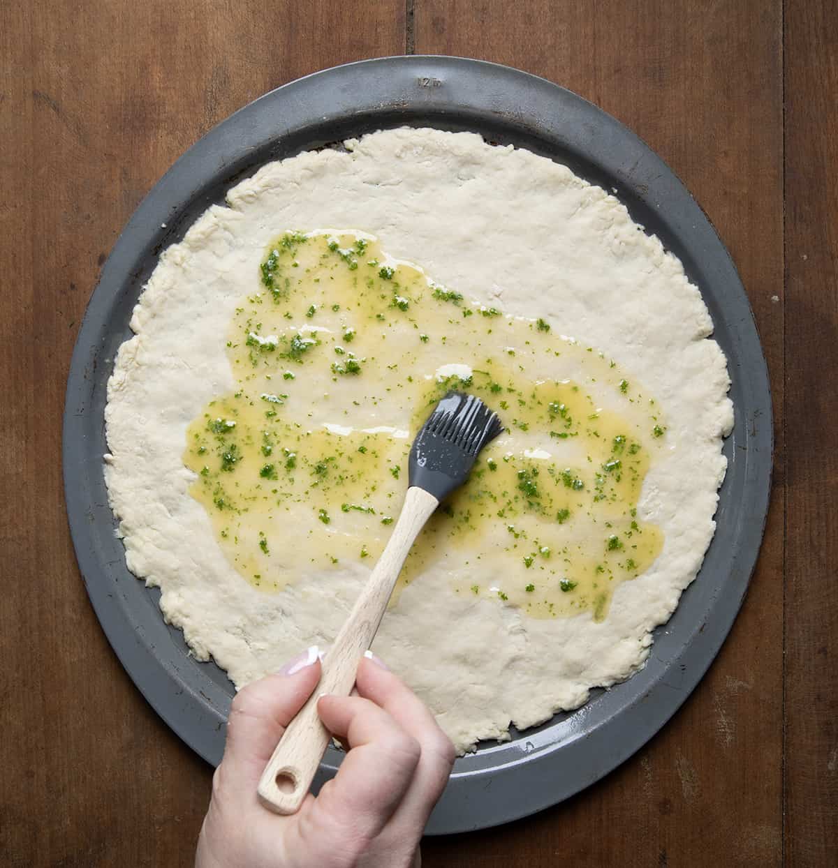Brushing herb butter over raw Bisquick Pizza Dough.