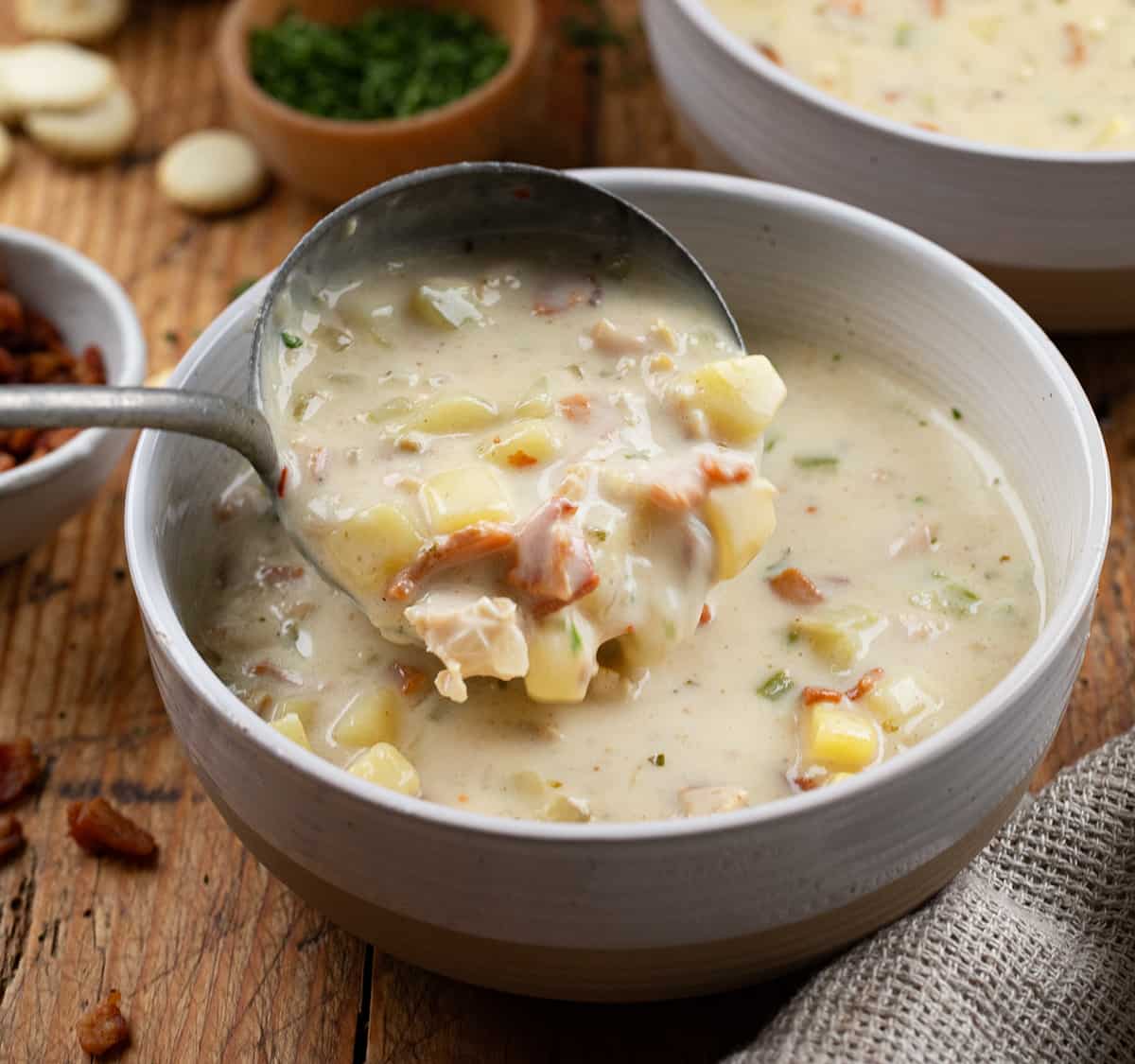 Pouring New England Clam Chowder into a bowl on a wooden table.