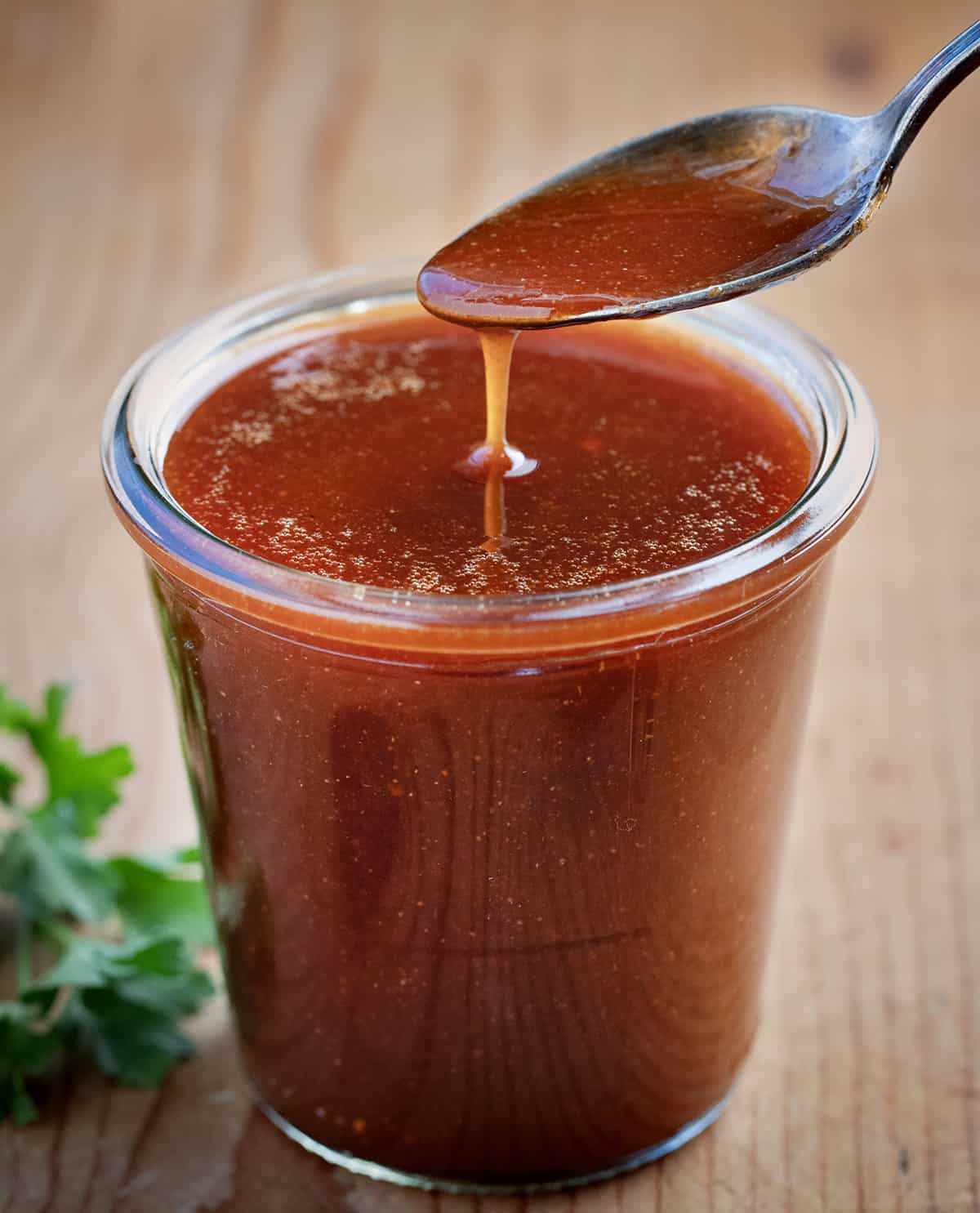 A spoon dipping into a jar of Firecracker Sauce on a wooden table.