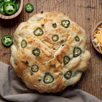Loaf of Jalapeno Cheddar Bread on a wooden cutting board near jalapeños and cheese.