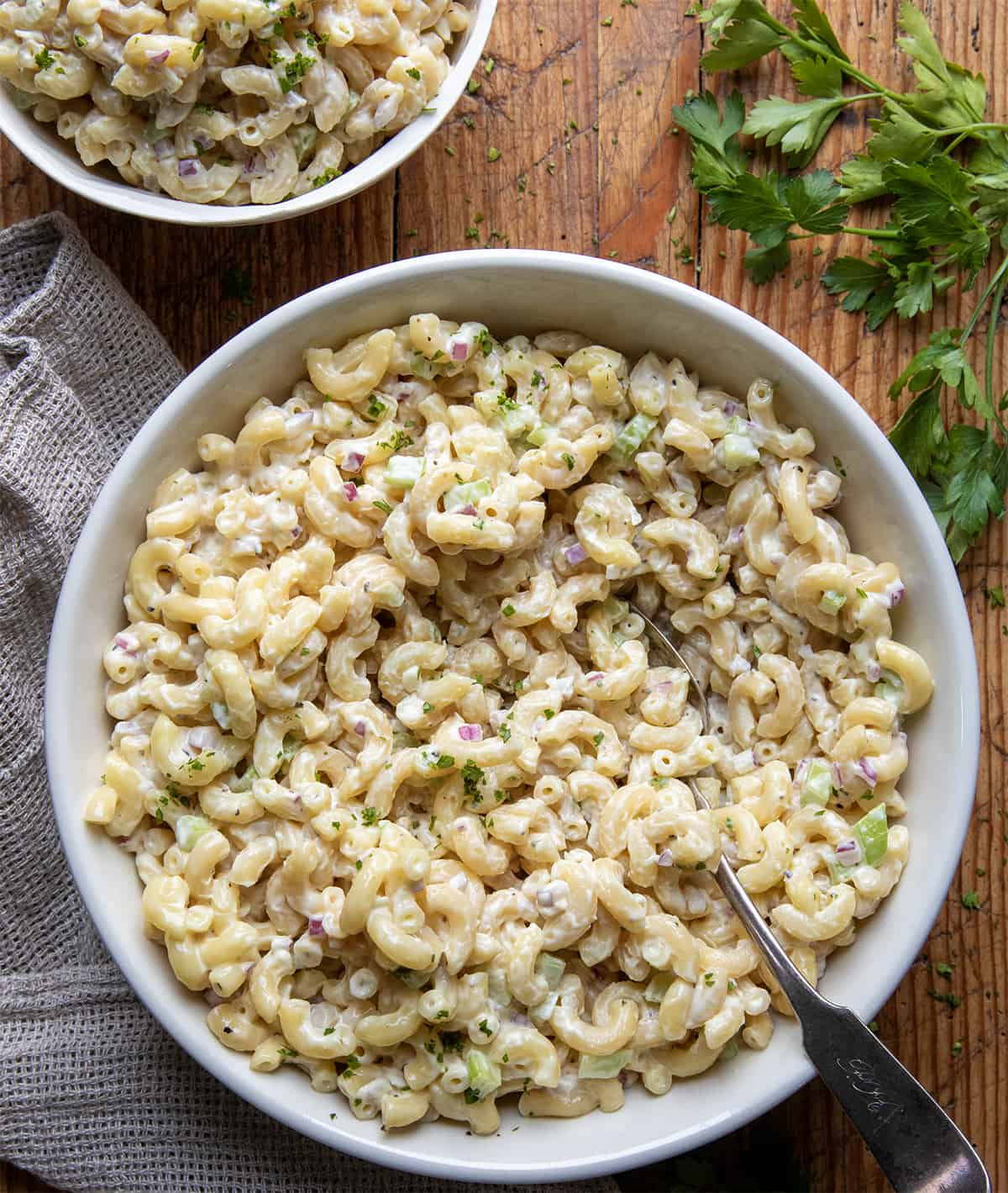 Macaroni Salad in a big bowl with a spoon on a wooden table.
