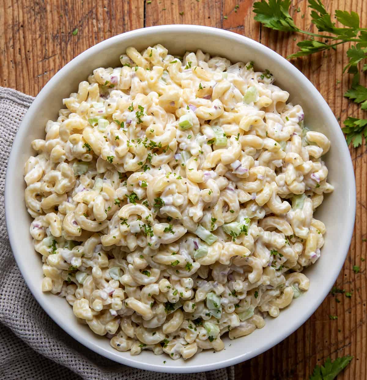 Macaroni Salad in a big white bowl on a wooden table.