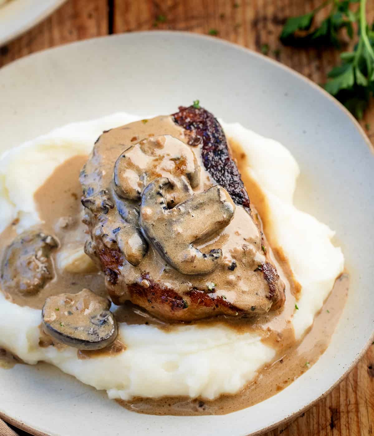 Piece of Creamy Mushroom Pork on a bed of mashed potatoes on a plate.