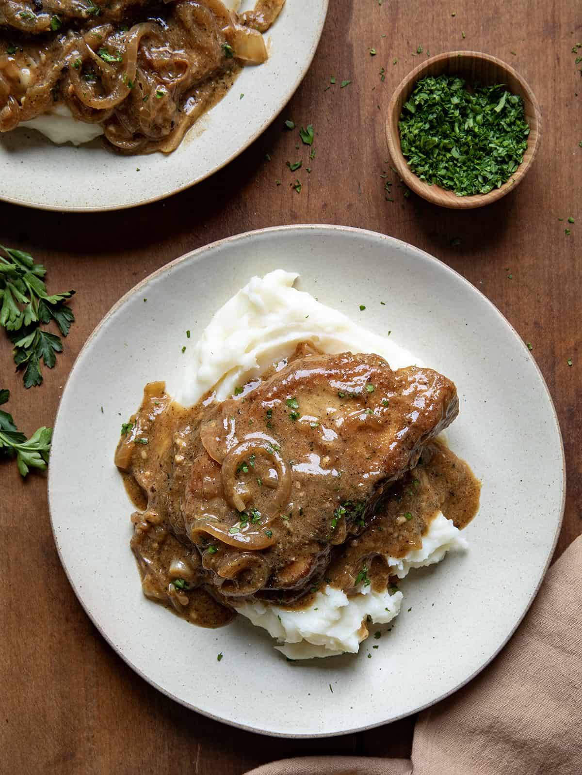 One Smothered Pork Chop on a bed of mashed potatoes on a plate.