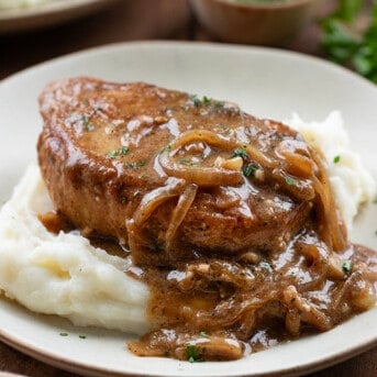 Piece of Smothered Pork Chops on a bed of mashed potatoes on a plate.