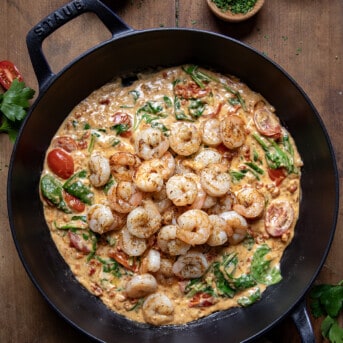 Creamy Tuscan Shrimp in a pan with the shrimp on top of the sauce on a wooden table.