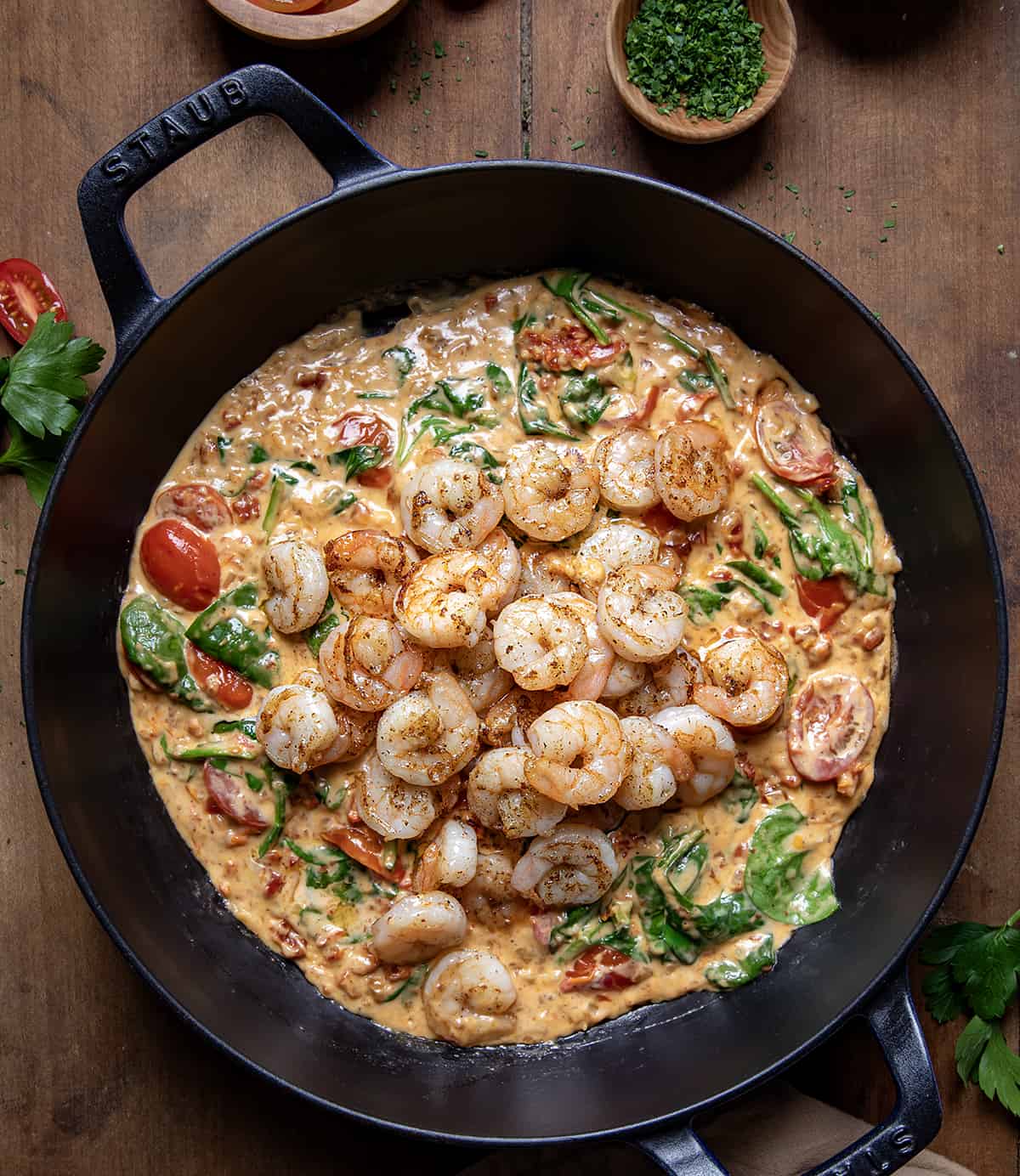 Creamy Tuscan Shrimp in a pan with the shrimp on top of the sauce on a wooden table.
