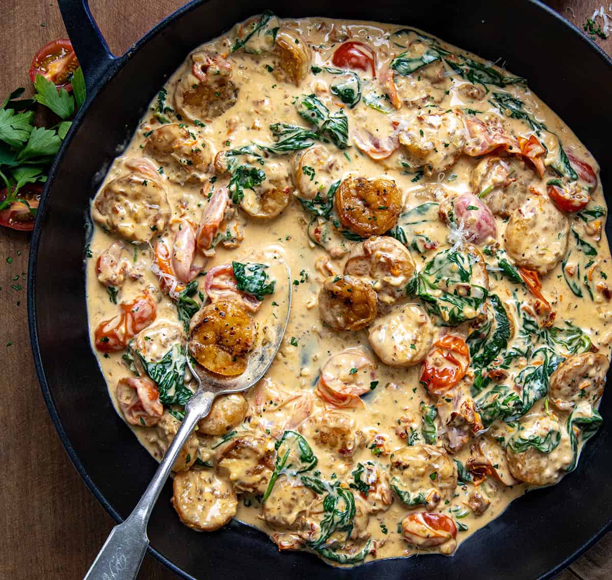 Pan of Creamy Tuscan Shrimp on a wooden table with a spoon from overhead.