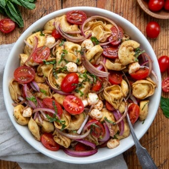 Bowl of Caprese Tortellini Pasta Salad on a wooden table with a spoon.