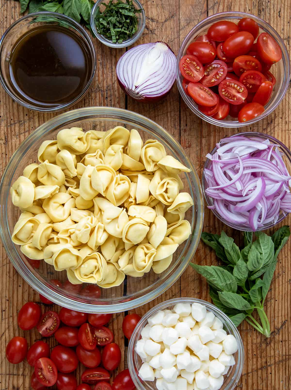 Ingredients used to make Caprese Tortellini Pasta Salad on a wooden table.
