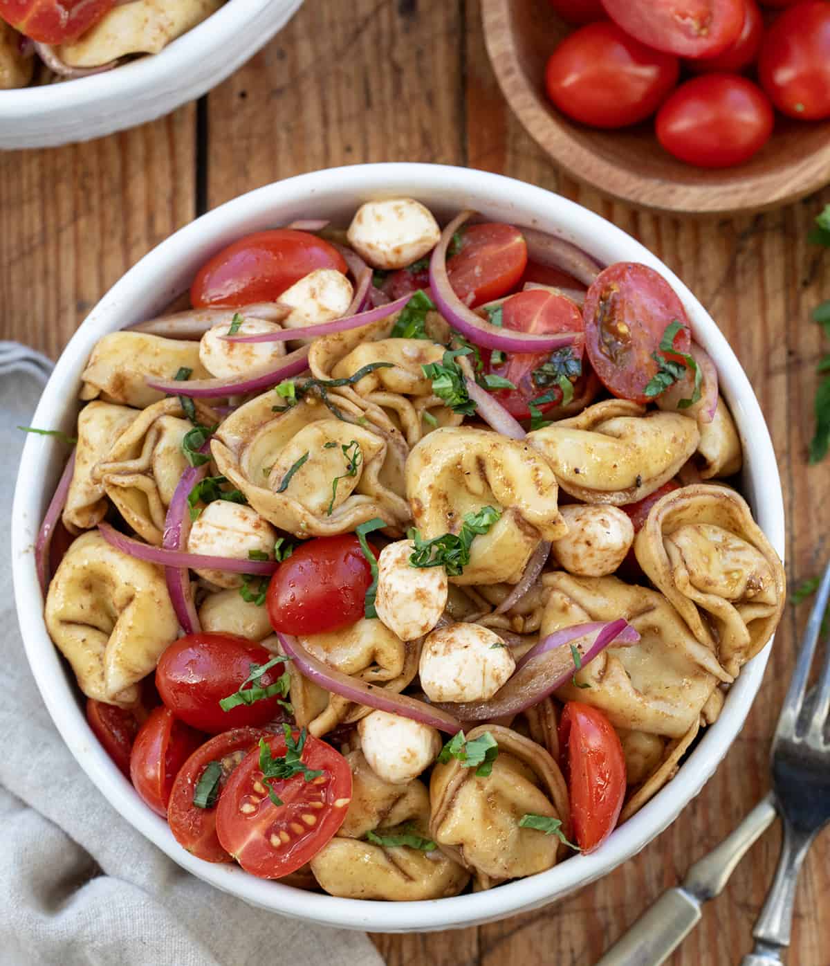 Bowls of Caprese Tortellini Pasta Salad on a wooden table.