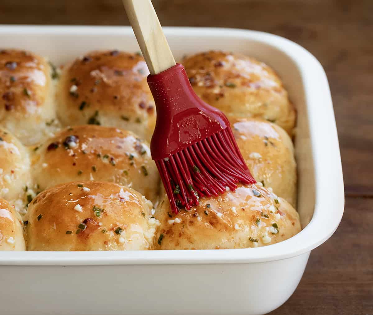Brushing butter on Cheesy Garlic Dinner Rolls in a pan.