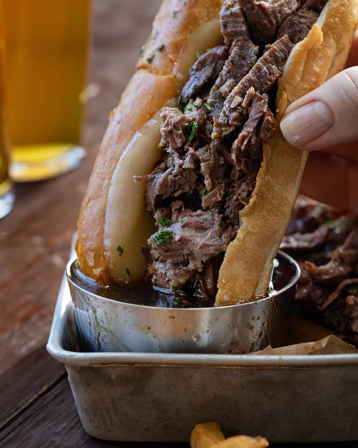 Dipping French Dip sandwich into cup of Au Jus with beer in the background.