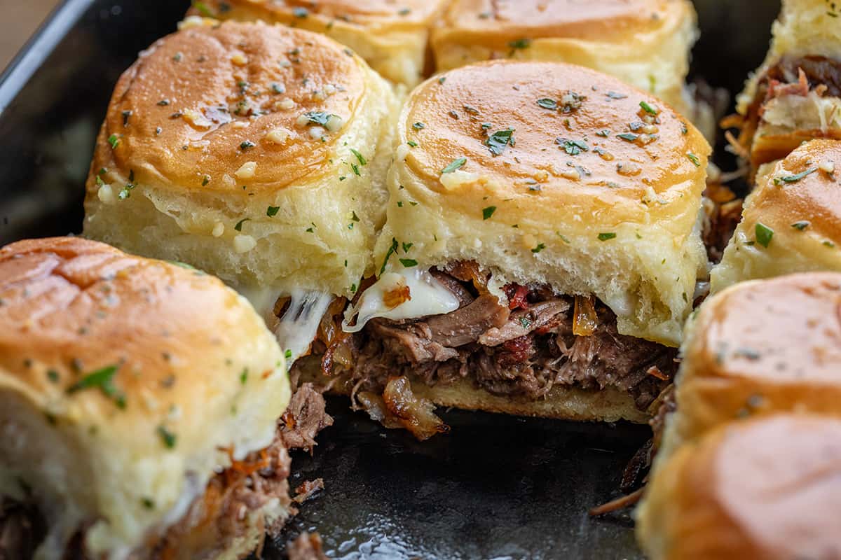 French Dip Sliders in a pan with a few sliders removed.