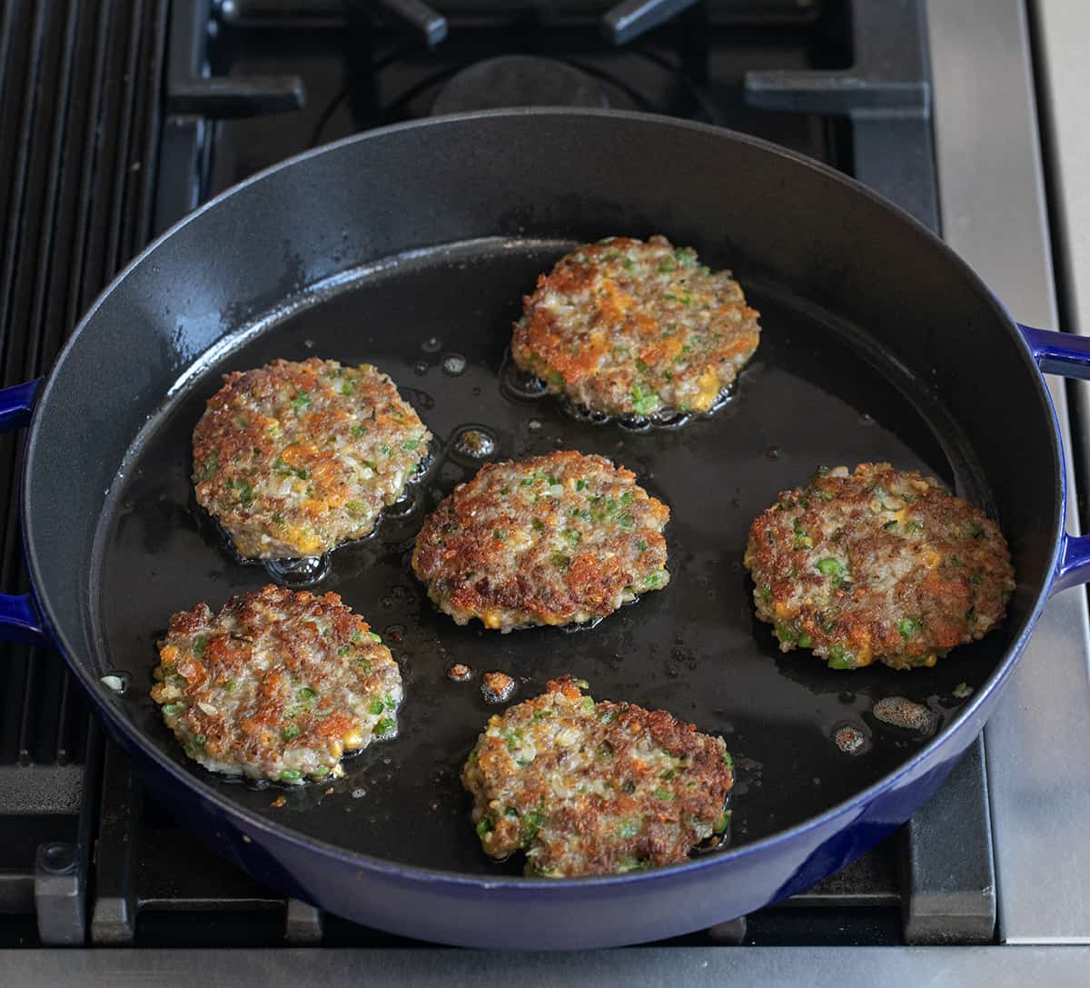 Jalapeno Cheese Sausage Patties in a skillet on a stovetop cooking.