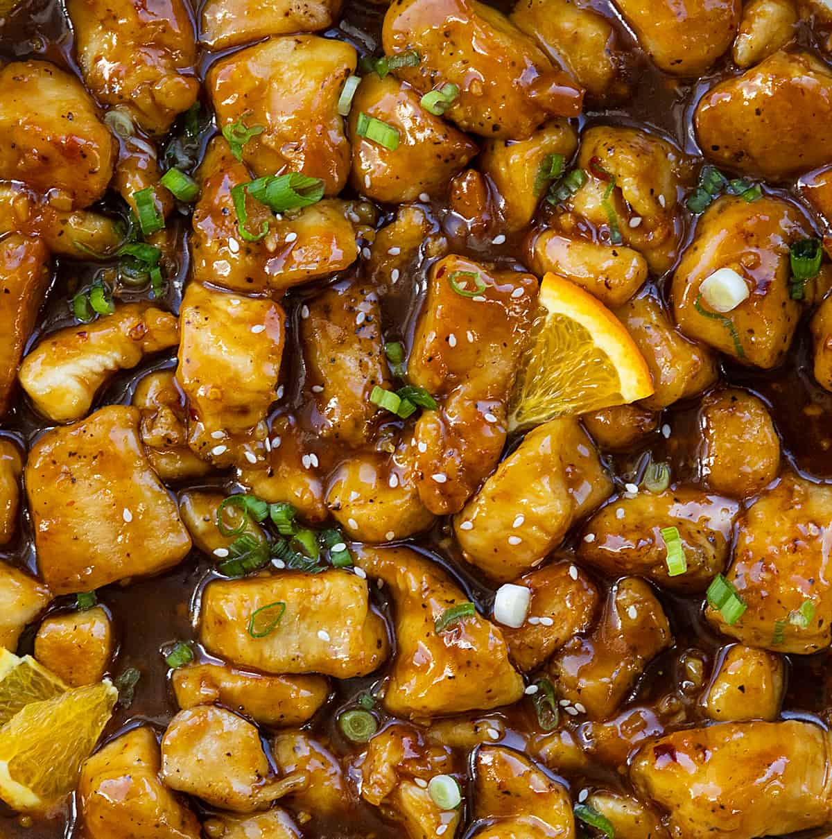 Close up of Orange Chicken in a pan with orange slices.