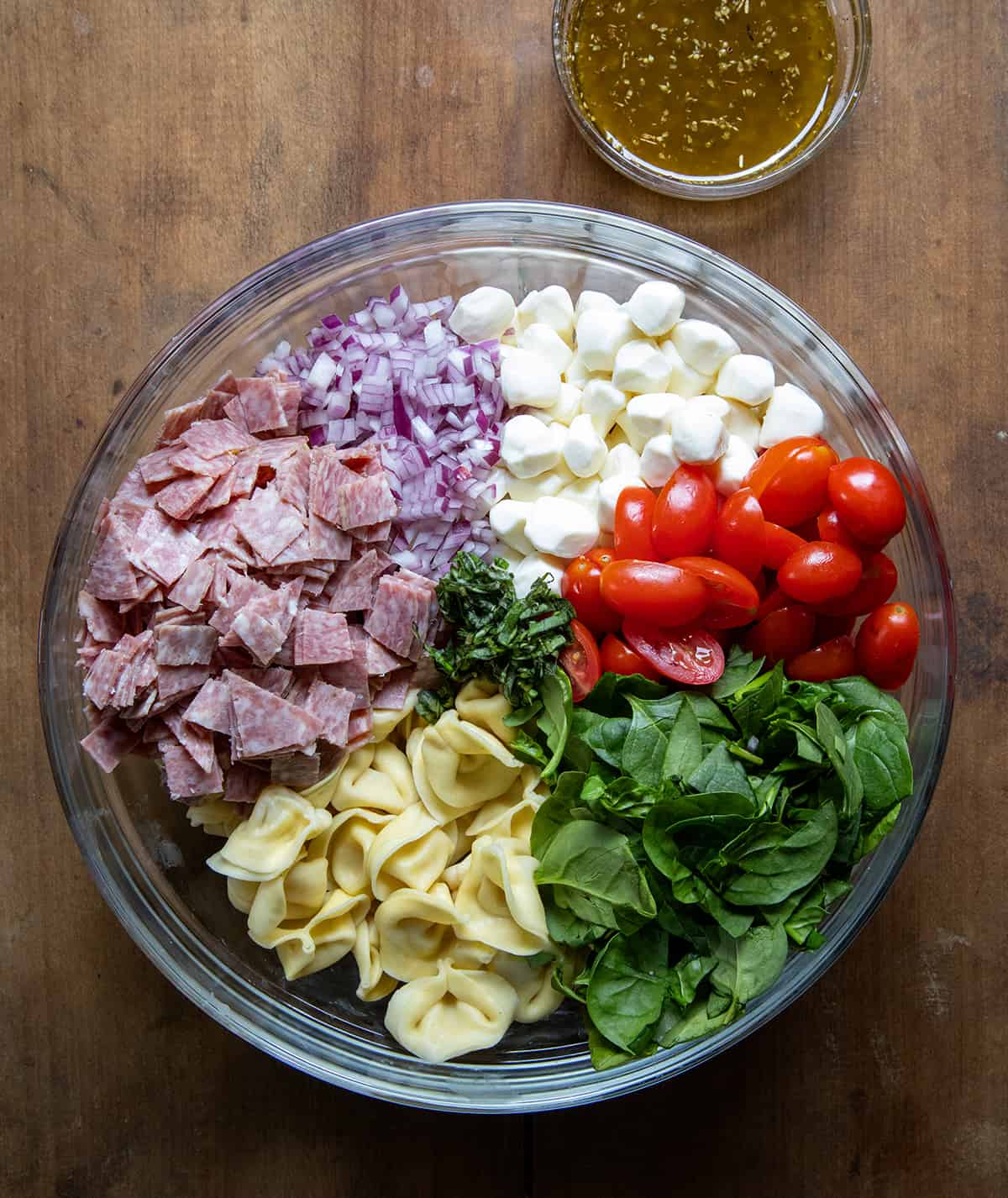 Raw ingredients for Tortellini Pasta Salad in a bowl on a table from overhead.