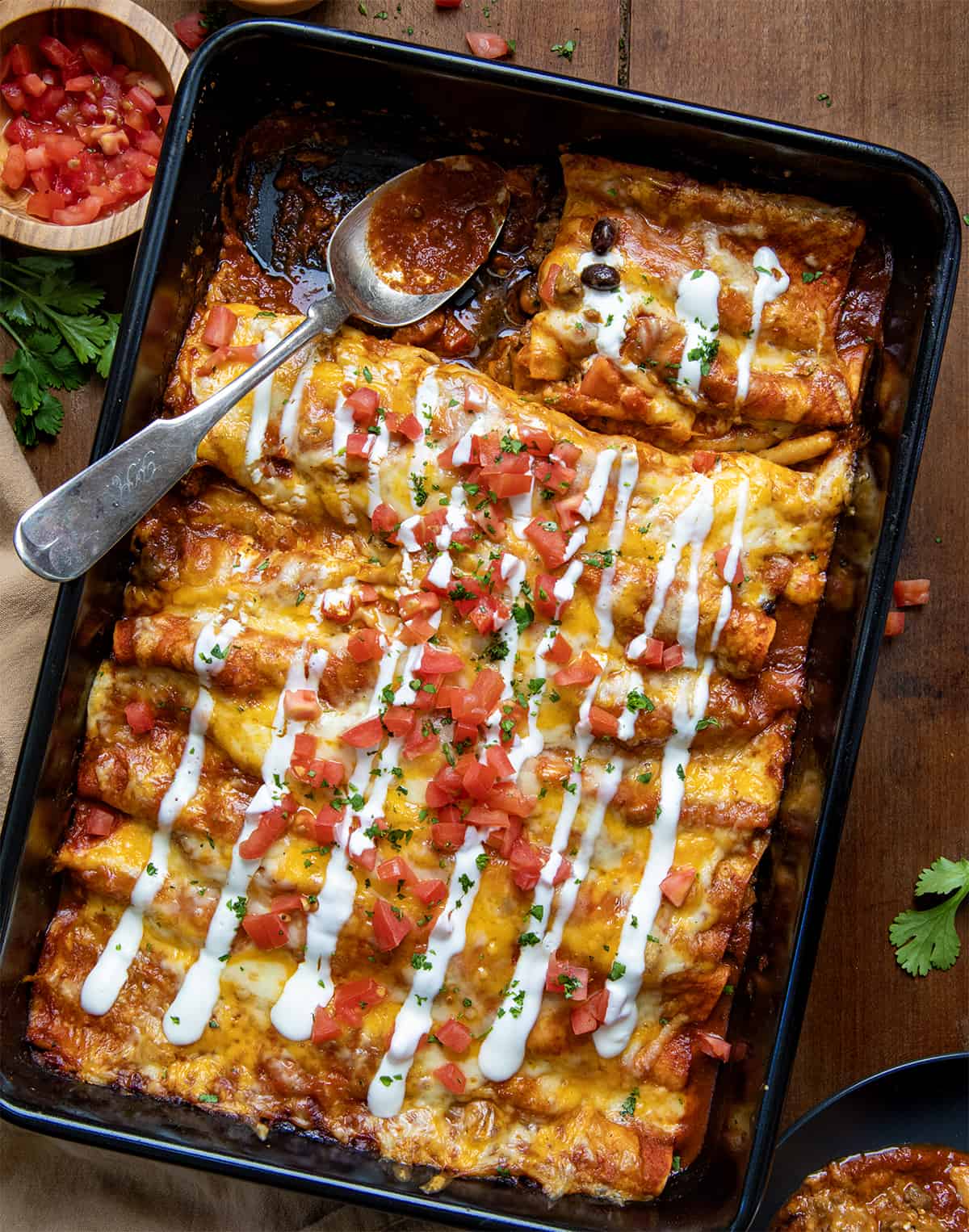 Beef Enchiladas in a pan with half of one removed on a wooden table. 