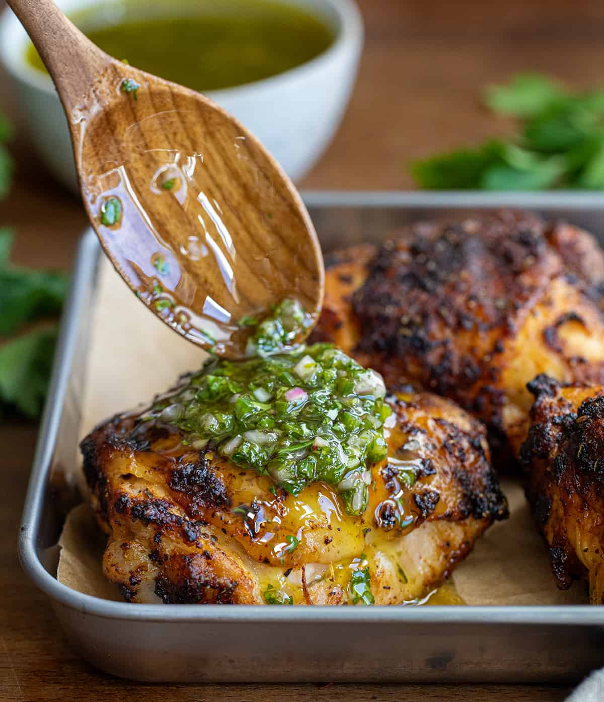 Drizzling chimichurri sauce over cooked chicken thighs.