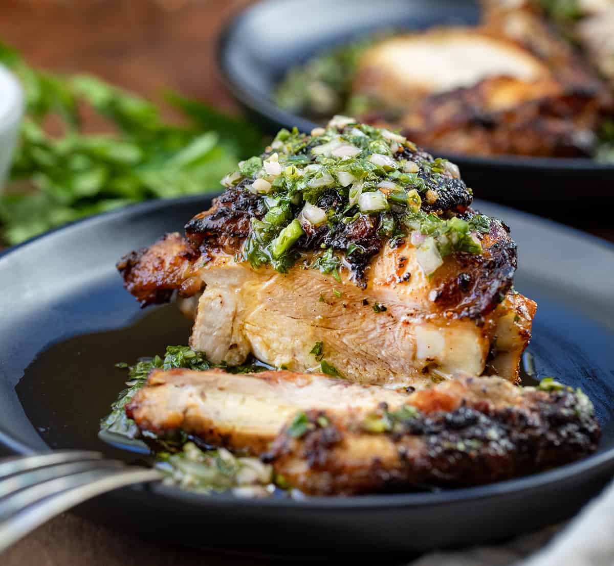 Piece of Chimichurri Chicken on a black plate cut into showing tender chicken thigh.