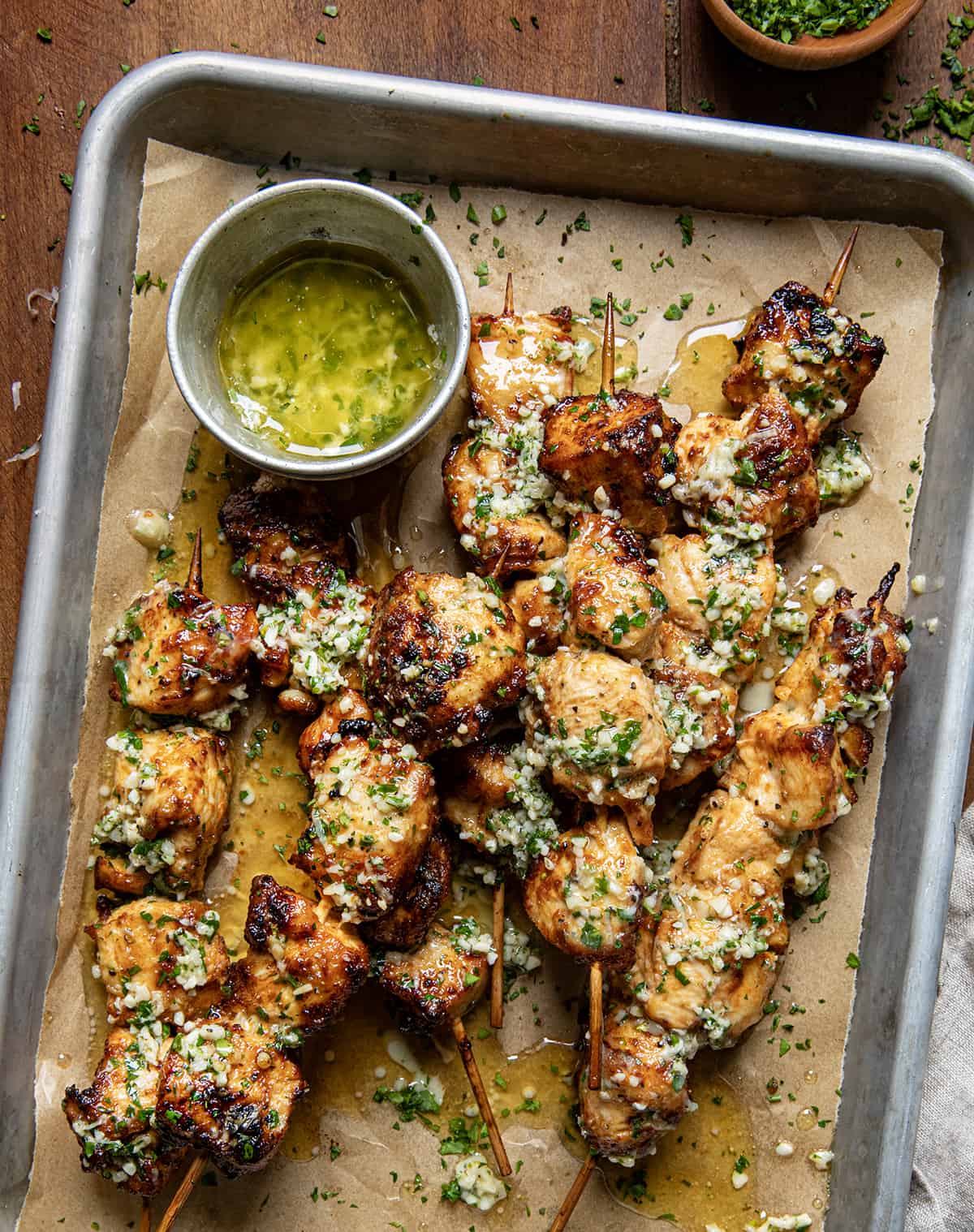 Pan of Garlic Parmesan Chicken Skewers with garlic butter on a wooden table from overhead.