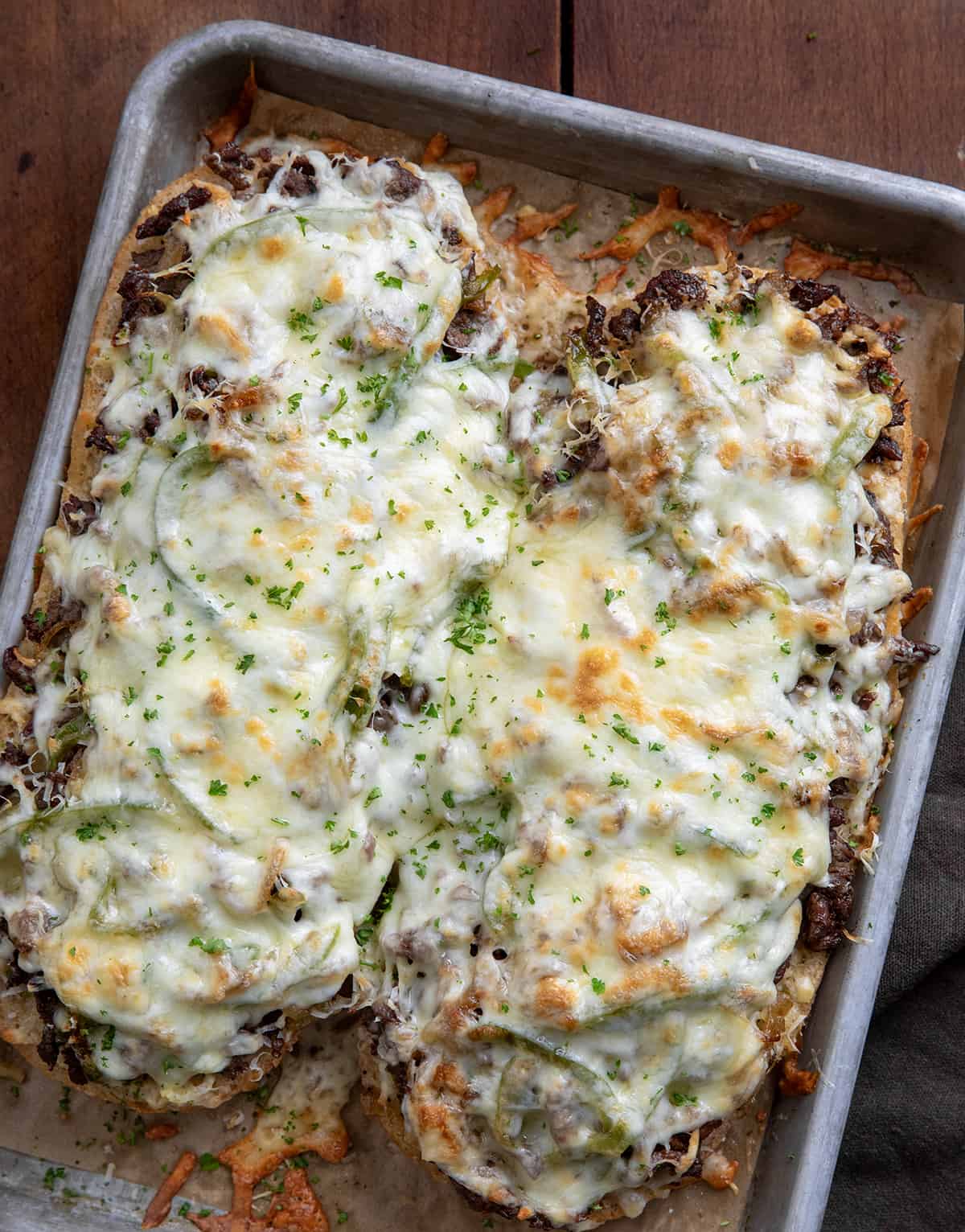 Philly Cheesesteak Garlic Bread on a sheet pan on a wooden table from overhead.