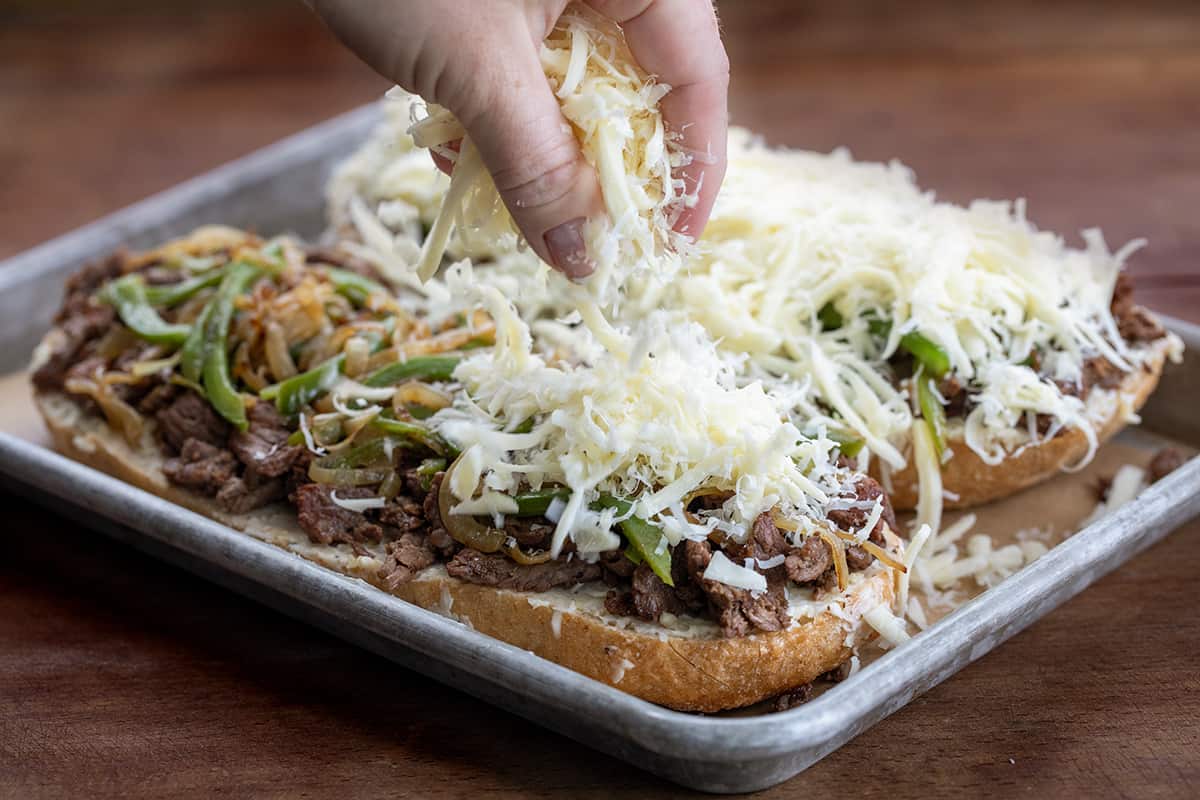 Spreading cheese over Philly Cheesesteak Garlic Bread before baking.