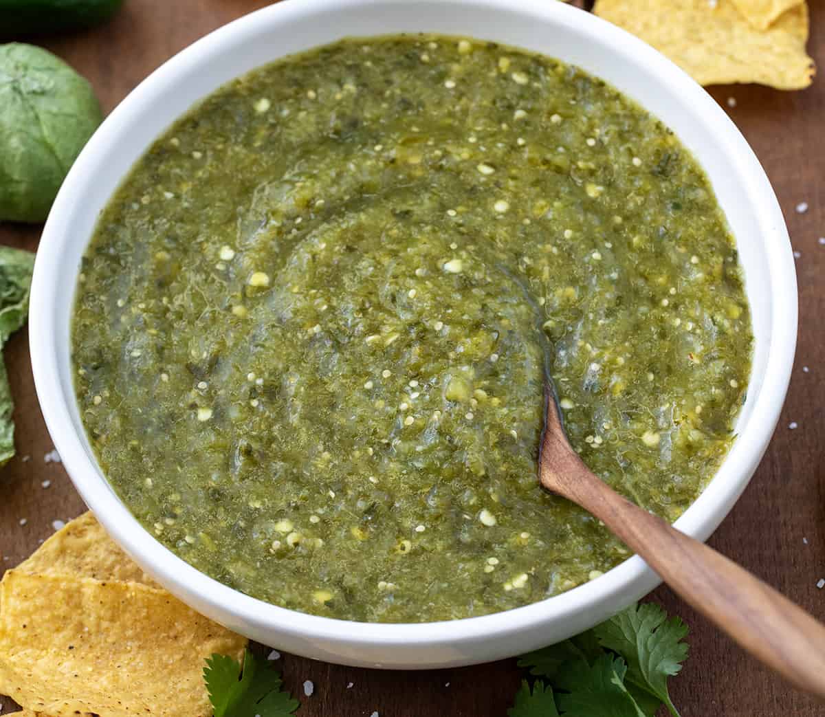 Bowl of Salsa Verde on a wooden table with chips from overhead.