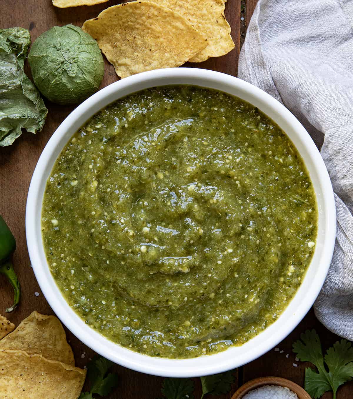 Bowl of Salsa Verde on a wooden table with chips from overhead. 