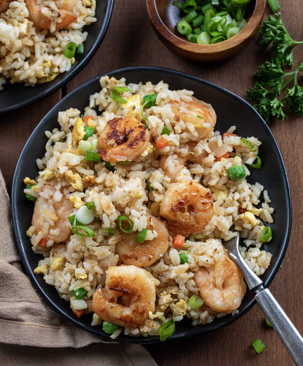Plates of Shrimp Fried Rice on a wooden table with a fork.