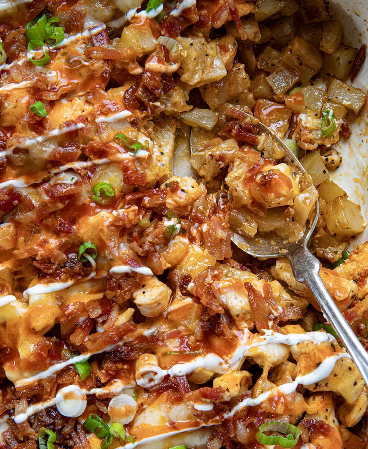 Close up of Buffalo Chicken Roasted Potato Bake in casserole pan showing potatoes, chicken, cheese, bacon, and onion.