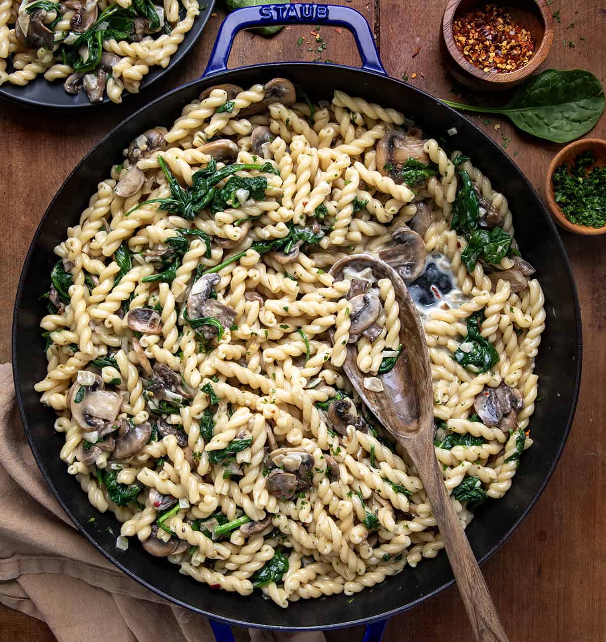 Skillet of Creamy Mushroom and Spinach Pasta with a wooden spoon in it from overhead.