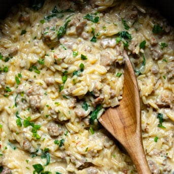 Close up of One Pot Sausage Orzo inside the pot with a wooden spoon.
