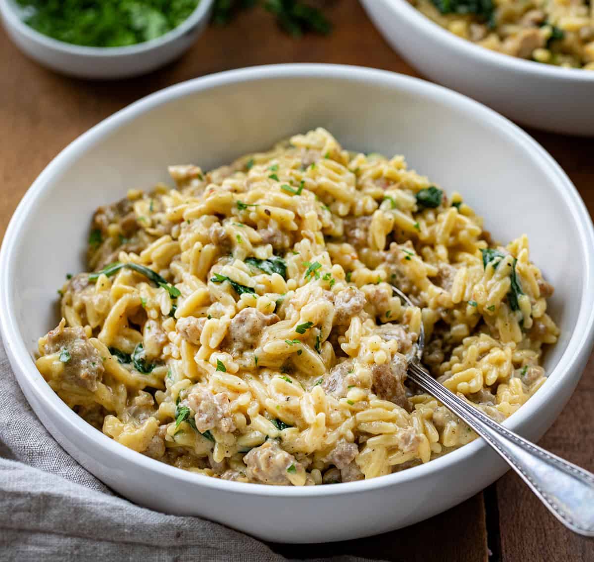 One Pot Sausage Orzo on a wooden table with a spoon close up.