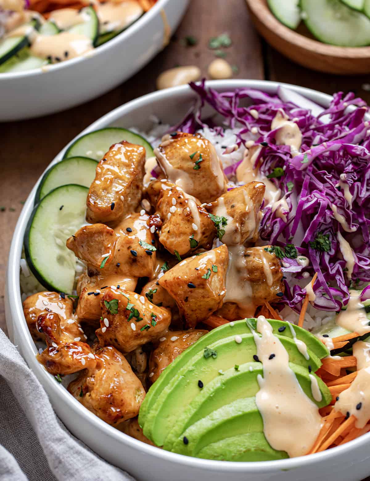 Close up of a bowl of Bang Bang Chicken with avocado, cabbage, cucumber, and carrot.