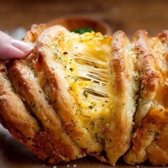 Hand pulling away some From Scratch Cheesy Garlic Pull-Apart Bread.