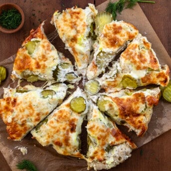 Dill Pickle Focaccia Bread on a piece of parchment paper cut into slices like a pizza.