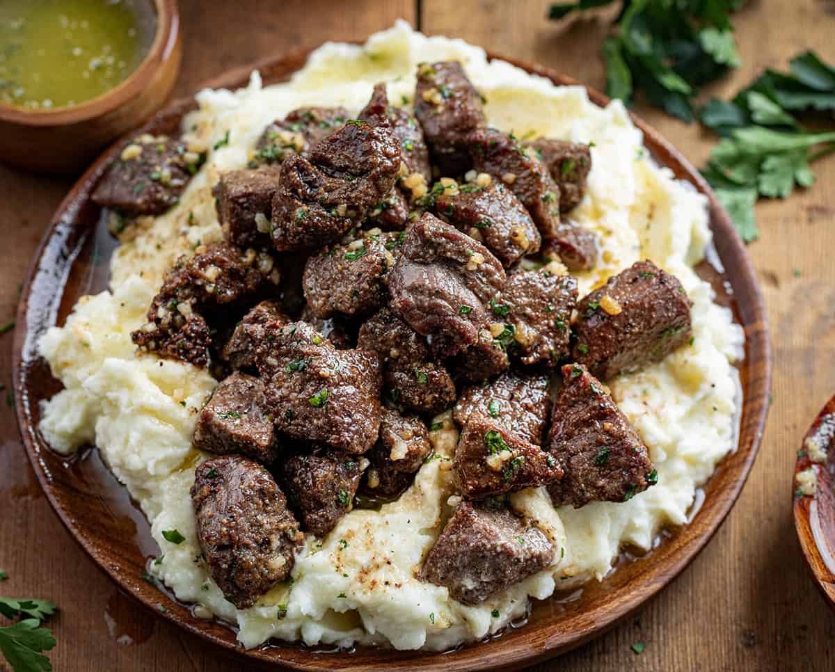 Plate of Air Fryer Garlic Butter Steak Bites on mashed potatoes on a wooden table.