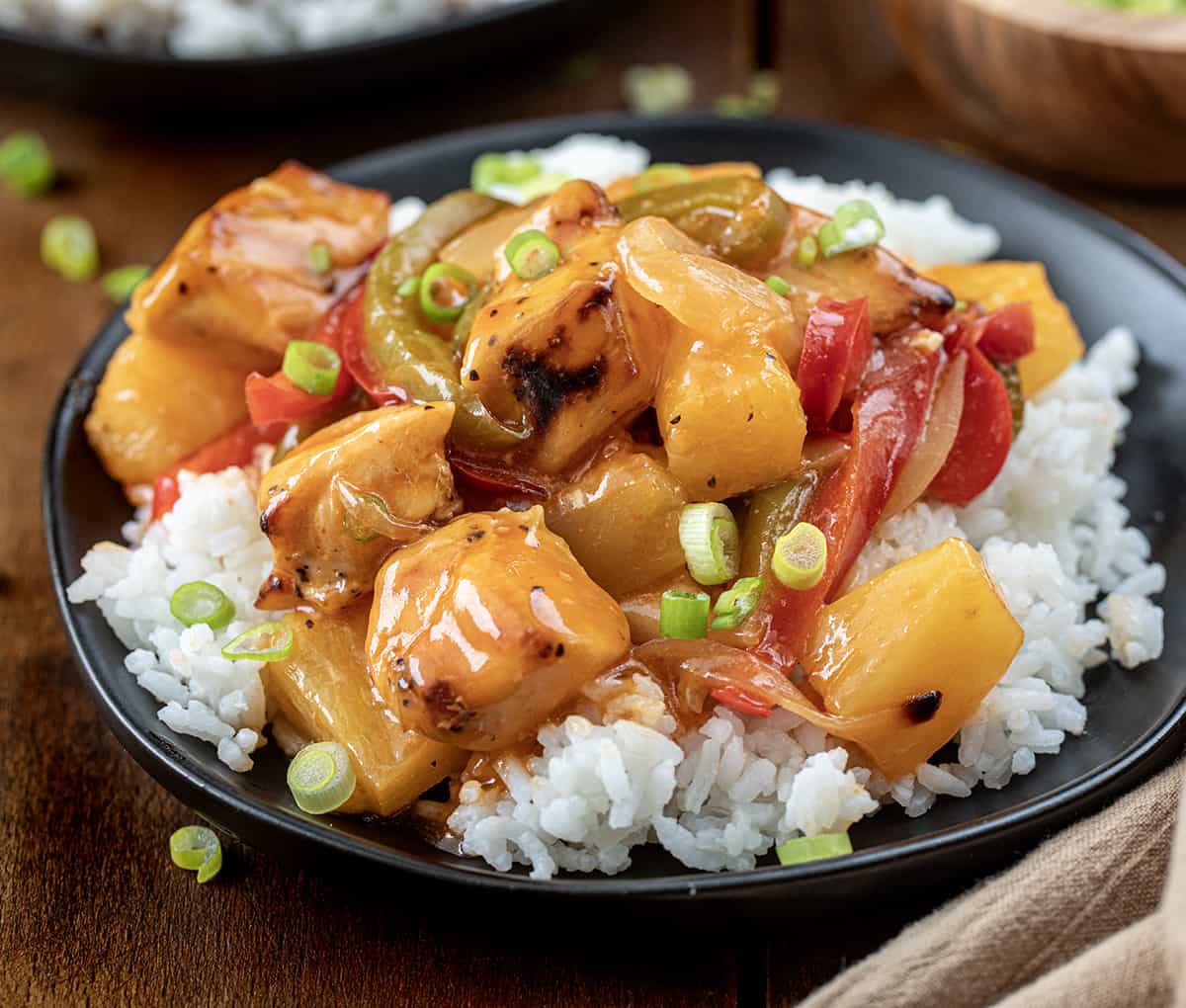 Plate of Sweet and Sour Chicken Sheet Pan Meal over rice on a black plate.