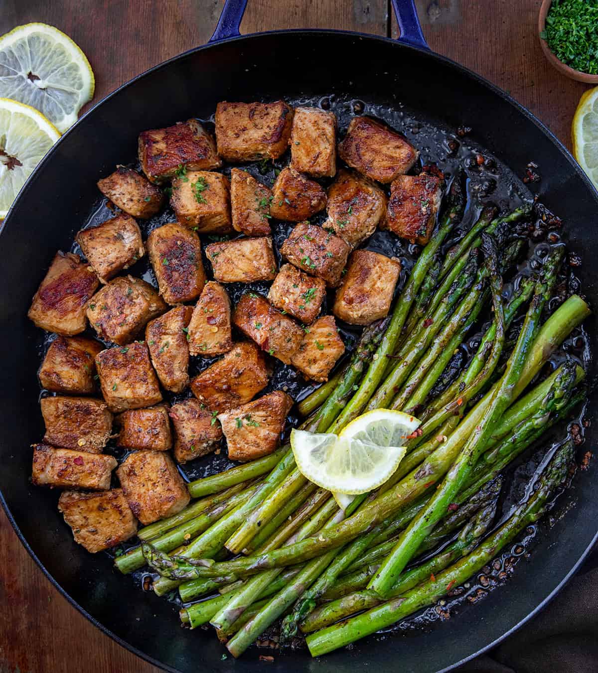 Skillet filled with Blackened Pork Bites and Asparagus on a wooden table from overhead.