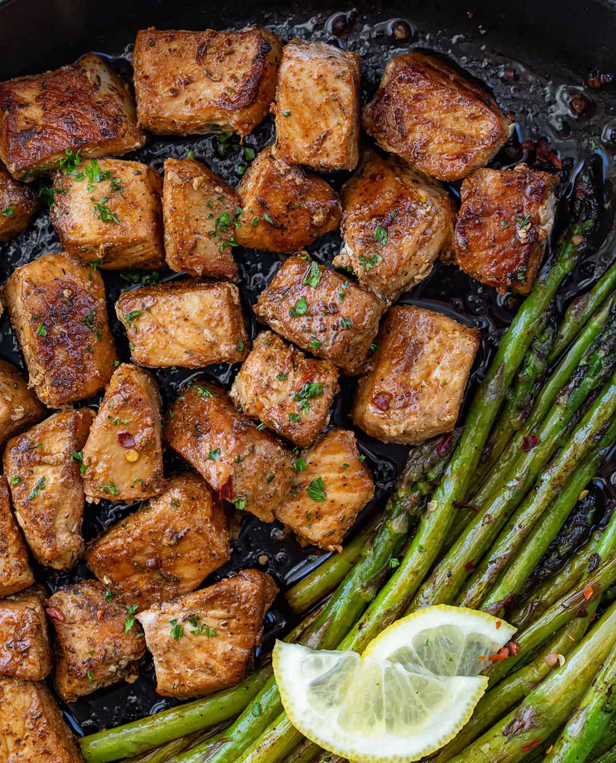 Skillet filled with Blackened Pork Bites and Asparagus on a wooden table from overhead. 