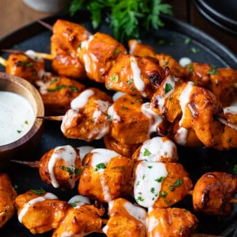 Buffalo Ranch Chicken Skewers on a platter with ranch dressing drizzled over top.