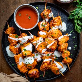 Buffalo Ranch Chicken Skewers on a platter with buffalo sauce and ranch dressing drizzled over top.