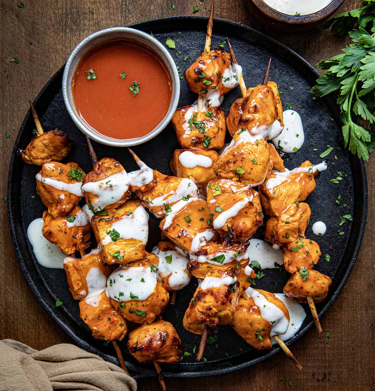 Buffalo Ranch Chicken Skewers on a platter with buffalo sauce and ranch dressing drizzled over top. 
