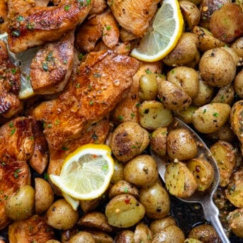 Close up of cooked chicken and baby potatoes with lemon slices.