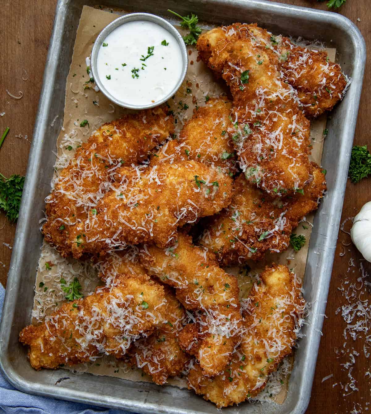 Pan of Garlic Parmesan Chicken Tenders on a wooden table with some ranch dressing from overhead.