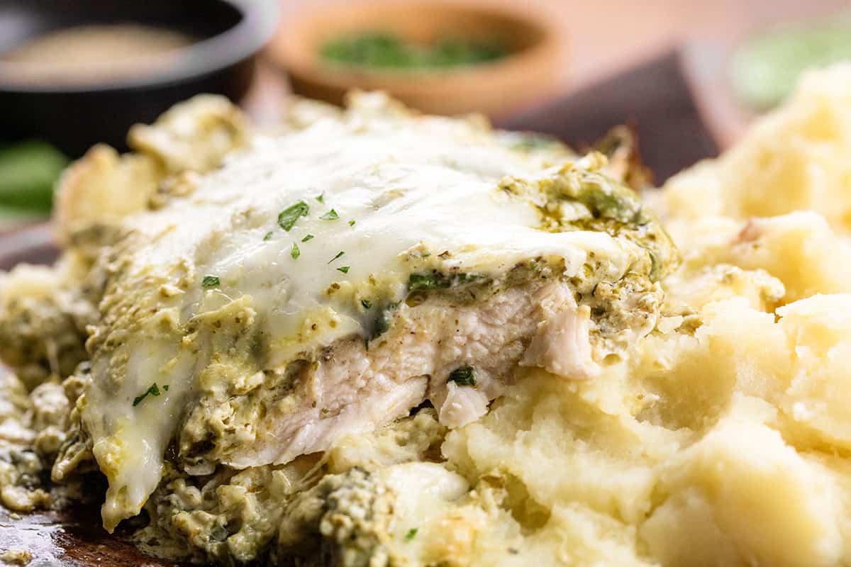 Cut up piece of Cheesy Pesto Chicken on a bed of mashed potatoes.