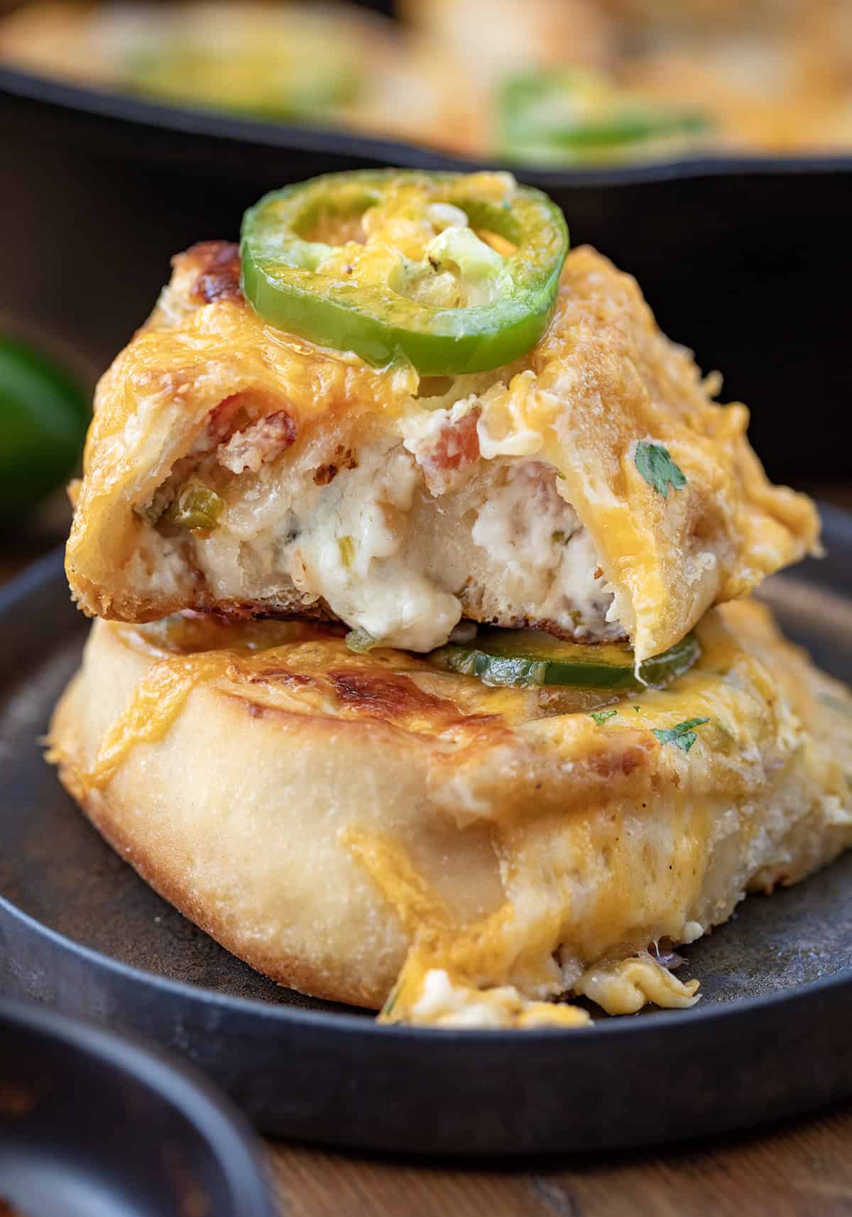 Jalapeno Popper Skillet Rolls stacked on a plate with top roll with a bite taken out of it.